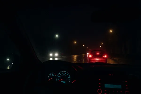 Wide nighttime view from inside a car with dark tinted windows, showing poor visibility of the wet road, oncoming headlights, and dim streetlights.